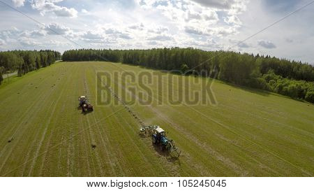 Two tractors collect hay on field near forest at summer sunny day. Aerial view videoframe