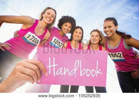 The word handbook and hand holding card against five smiling runners supporting breast cancer marathon