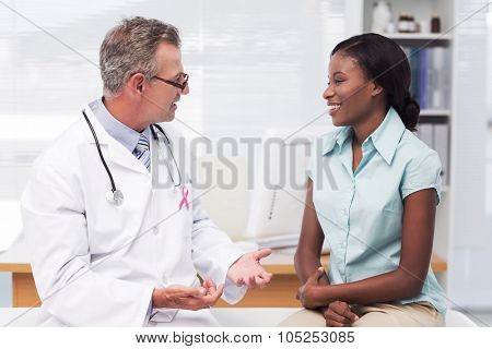 Pink awareness ribbon against doctor speaking with cheerful young patient