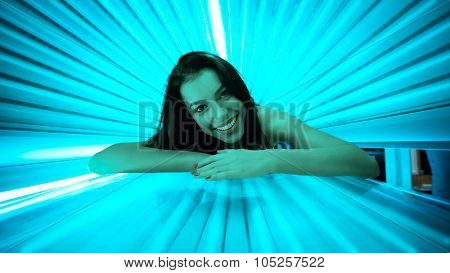 Smiling young woman laying on solarium, tanning skin treatment