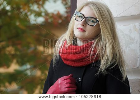 Blonde young woman in black and white cat eye glasses and red leather gloves posing at autumn yellow