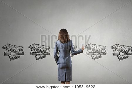 Back view of businesswoman drawing money banknotes on wall