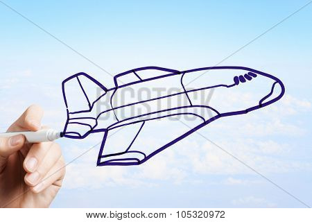 Person drawing airplane model on sky background