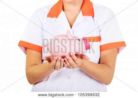 Young female doctor or nurse holding a piggybank.