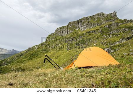 Orange tent in the mountains and trekking pole