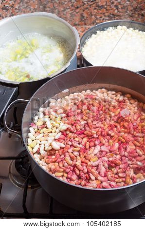 Black cooking pot of white and red beans drained in water with some other pots around, preparation f