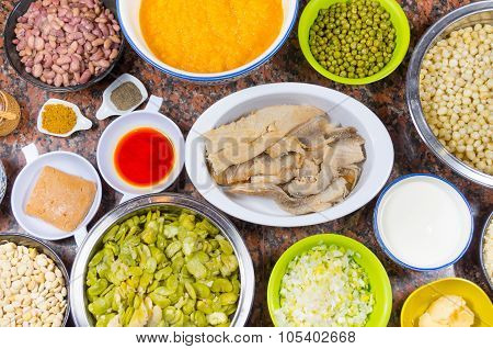 Bowls of different ingredients spread out on granite surface including green peas, onions, abbas, co