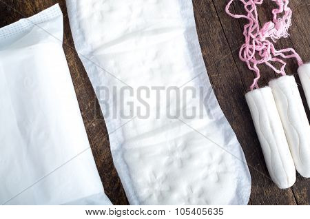 Sanitary pads for women with clean white tampons lying on top of wooden surface, shot from above ang