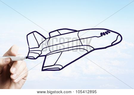 Person drawing airplane model on sky background
