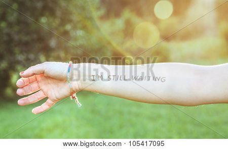 Female arm with text -I'm still waiting- written in skin