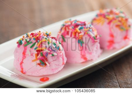 Pink ice cream on plate, decor with colorful rice, on old wooden vintage table background.