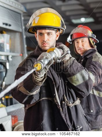 Confident male firefighters spraying water during training at fire station