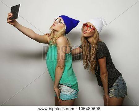 two hipster girls friends taking selfie with digital tablet, studio shot over gray vackground