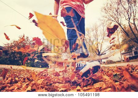 Child walking and kicking fall leaves. Focus on jeans and background leaves. Motion blur. Instagram effect.