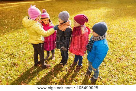 childhood, leisure, friendship and people concept - group of happy kids in autumn park counting and choosing game leader