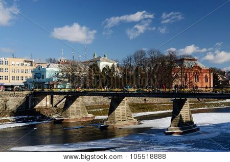 People crossing old pedestrian bridge over Uzh river in UzhhorodWestern Ukraine.City located at bord