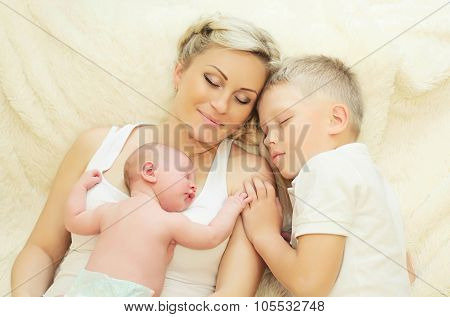 Mother With Two Children Sleeping Together On Bed At Home, Eldest Son And Youngest Baby