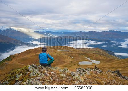 Morning landscape. Tourist in the mountains sits on a rock and looking over the valley. Overcast. Lake Koruldi. Main Caucasian ridge. Zemo Svaneti, Georgia 