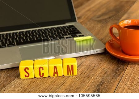 Scam written on a wooden cube in front of a laptop