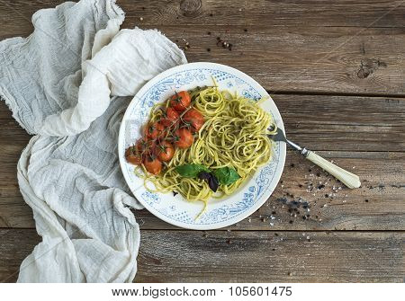 Pasta spaghetti with pesto sauce, basil, baked cherry-tomatoes on rustic wooden tabke dark table, to