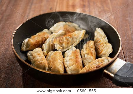 Close up cooking fried dumplings in a frying pan. Chinese food with hot steams, on rustic vintage wooden background. 
