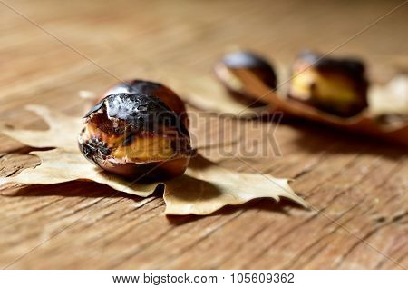 some roasted chestnuts, typical snack in All Saints Day in Catalonia, Spain, on some dry leaves on a rustic wooden surface