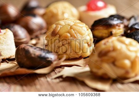 closeup of some roasted chestnuts and some panellets, typical snack in All Saints Day in Catalonia, Spain, and dry leaves on a rustic wooden surface
