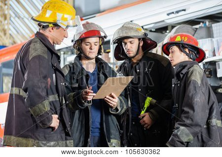 Male and female firefighters reading clipboard together at fire station