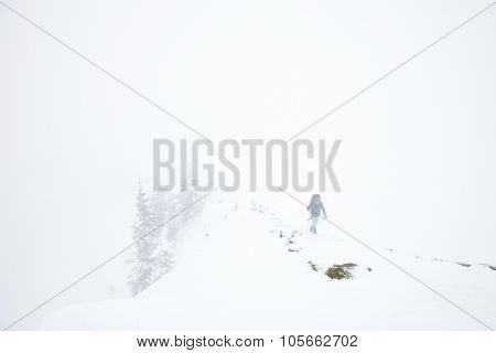 Male mountain climber with huge backpack and trekking poles having hard hiking trip during winter storm in Austrian Alps