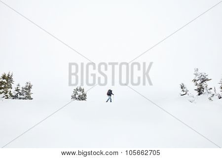 Male mountain climber with huge backpack and trekking poles having hard winter hiking trip after blizzard in Austrian Alps