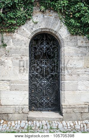 Old medieval black metal door with cerved bar and light stone wall.