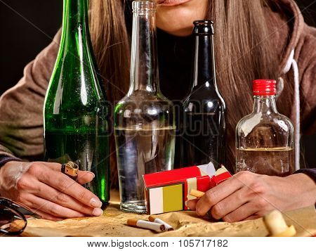 Girl  drinking alcohol and smokes cigarettes in solitude. Bottles and cigarettes in the foreground