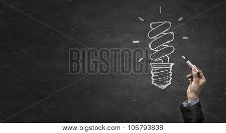 Human hand darwing light bulb as idea concept with chalk