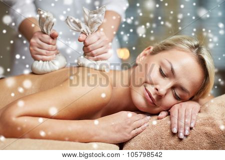 people, beauty, spa, winter and relaxation concept - close up of beautiful young woman lying and having herbal bag back massage in spa salon with snow effect