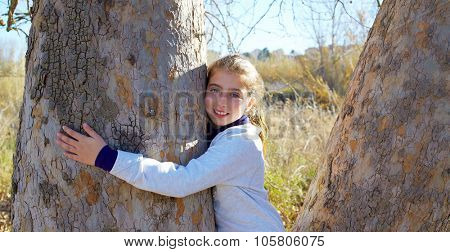 Kid girls loves nature hug a tree tunk in outdoor winter park