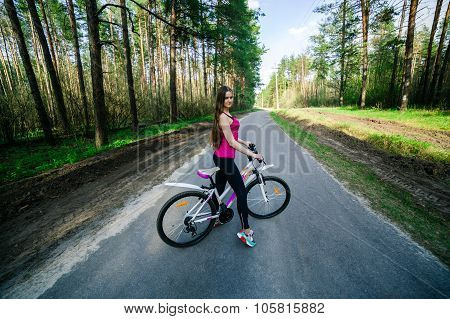 Young beautiful sports girl on a white bicycle in the woods