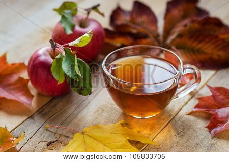 Glass Hot Cup Of Tea On A Wooden Table With Autumn Leaves And Apple