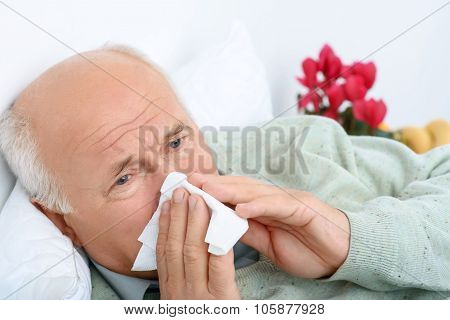 Sad exhausted old man is snorting at white handkerchief.