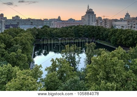 Park with Patriarshy pond among residential houses at summer evening