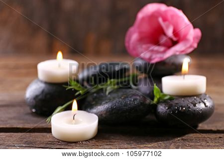 Alight candles, pebbles and fresh aroma flower composition on wooden background