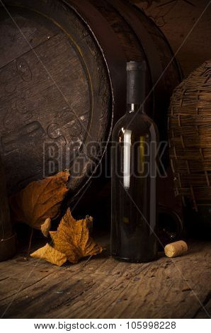 Still life with wine bottles, glasses and oak barrels.
