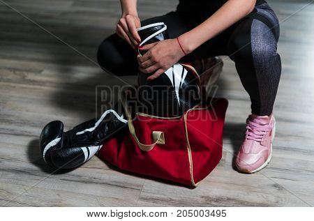 Young fighter boxer girl puting on boxing gloves before  training. She has sport bag