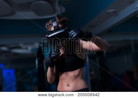 Young fighter boxer fit girl punching in VR glasses wearing boxing gloves in training. Boxing game in virtual reality 360 degrees. Futuristic gaming