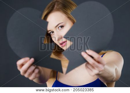 Depression sadness relationship problem concept. Young female with broken heart full of negative sad emotions. Woman covering her face by two parts of black love symbol.