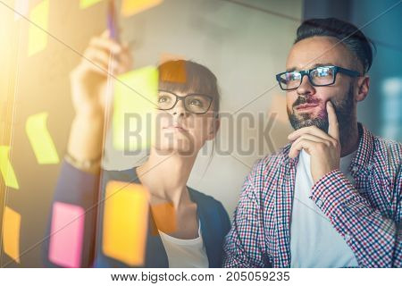 Business people meeting at office and use post it notes to share idea. Brainstorming concept. Sticky note on glass wall.