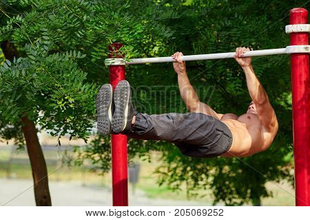 Full-length of strong athlete doing pull-up on horizontal bar. Mans fitness with blue sky in the background and open space around him.