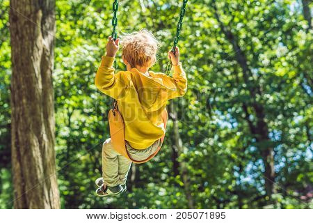 A boy in a yellow sweatshirt sits on a swing on a playground in autumn.