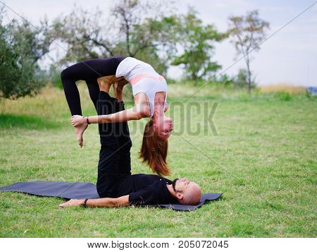 Beautiful woman and girl practise yoga pose outside. Women doing stretching workout in park outdoors at sunset.