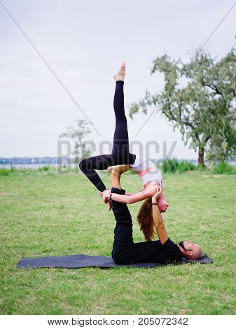 Beautiful woman and girl practise yoga pose outside. Women doing stretching workout in park outdoors at sunset.