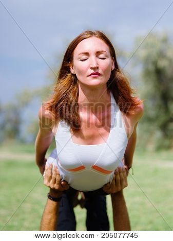 Girl in white shirt exercises yoga outdoor, on green grass.